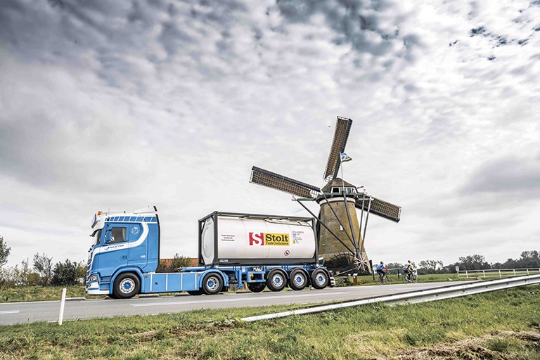 Truck loaded with tank container driving next to a windmill
