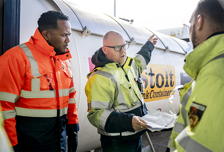 Three men in safety gear discussing state of a tank container